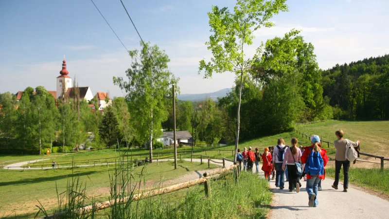 Group of children with adults on a hiking trail, castle and green landscape in the background