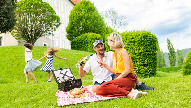 Couple on a picnic blanket on a green meadow, behind them a castle and two dancing children