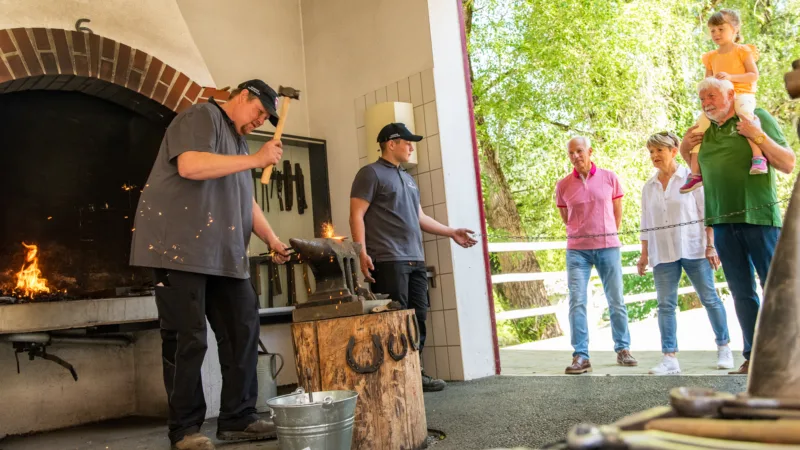 Man at work in a blacksmith's workshop, elderly couple with child watching