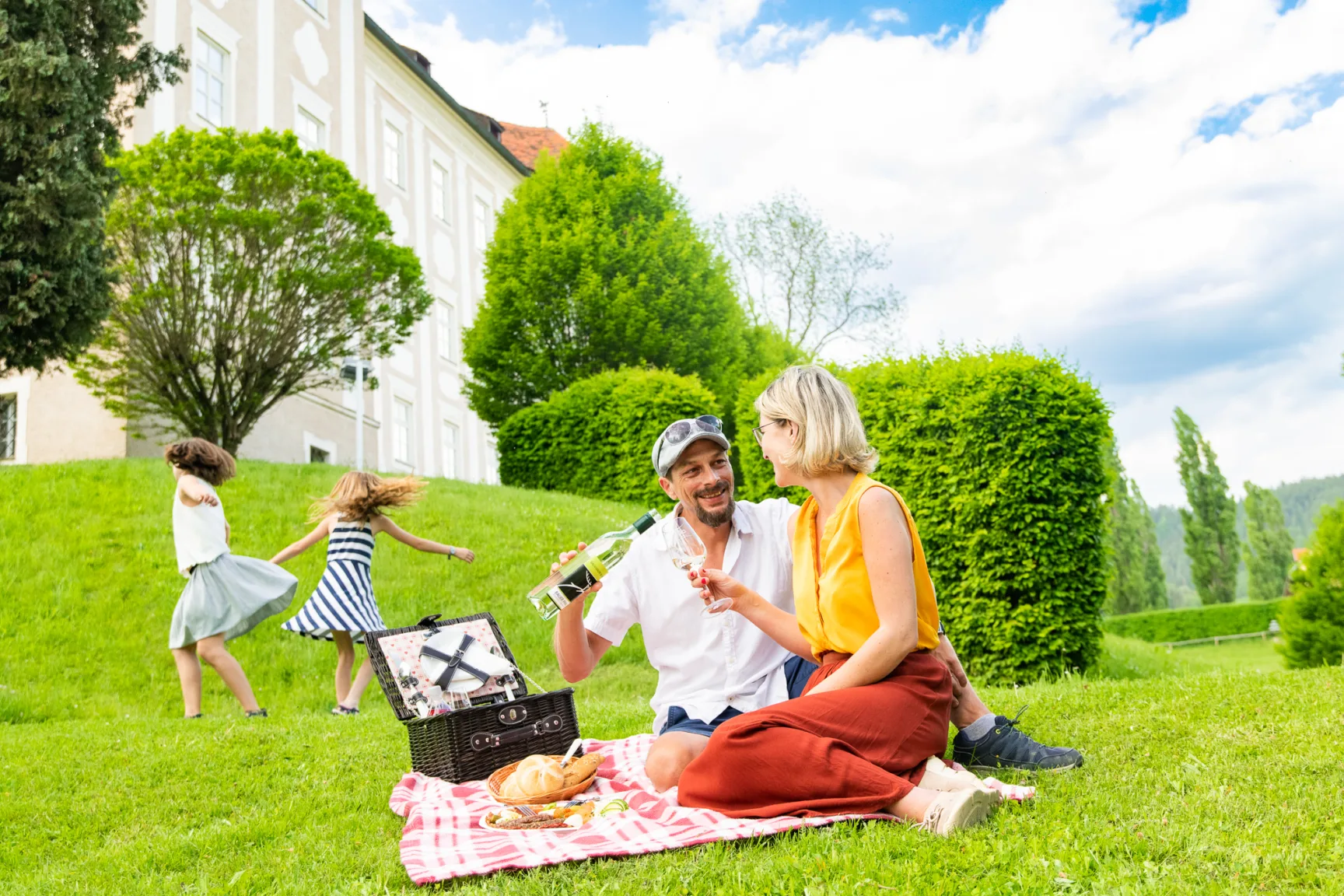 Couple on a picnic blanket on a green meadow, behind them a castle and two dancing children