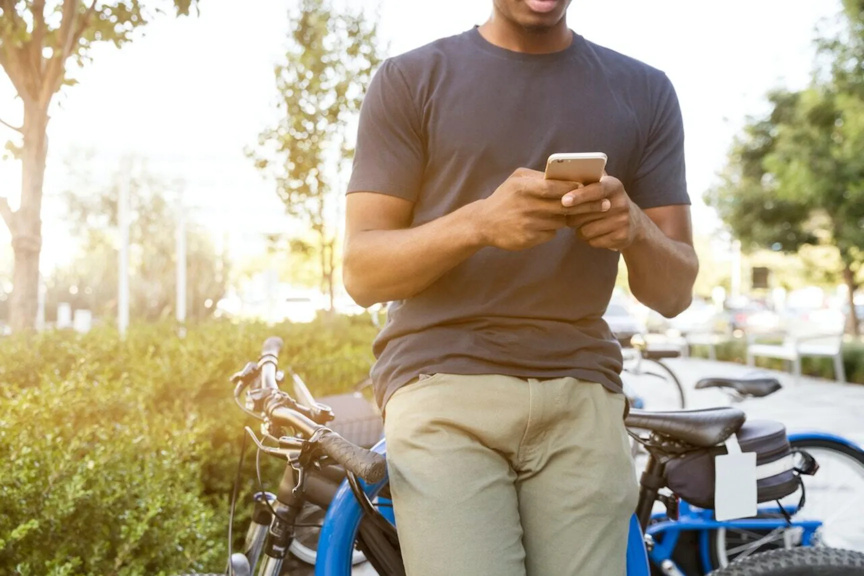 Man leaning on a bicycle with a smartphone in his hands, a park and sunshine in the background