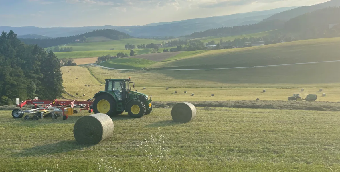 Green tractor and hay bales on a field during hay harvest in the sunshine