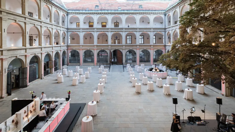 Überdachte Stallburg der Spanischen Hofreitschule, ein Renaissancegebäude mit offenen Arkaden auf zwei Stockwerke. Stehtische in der Mitte und eine Bar.