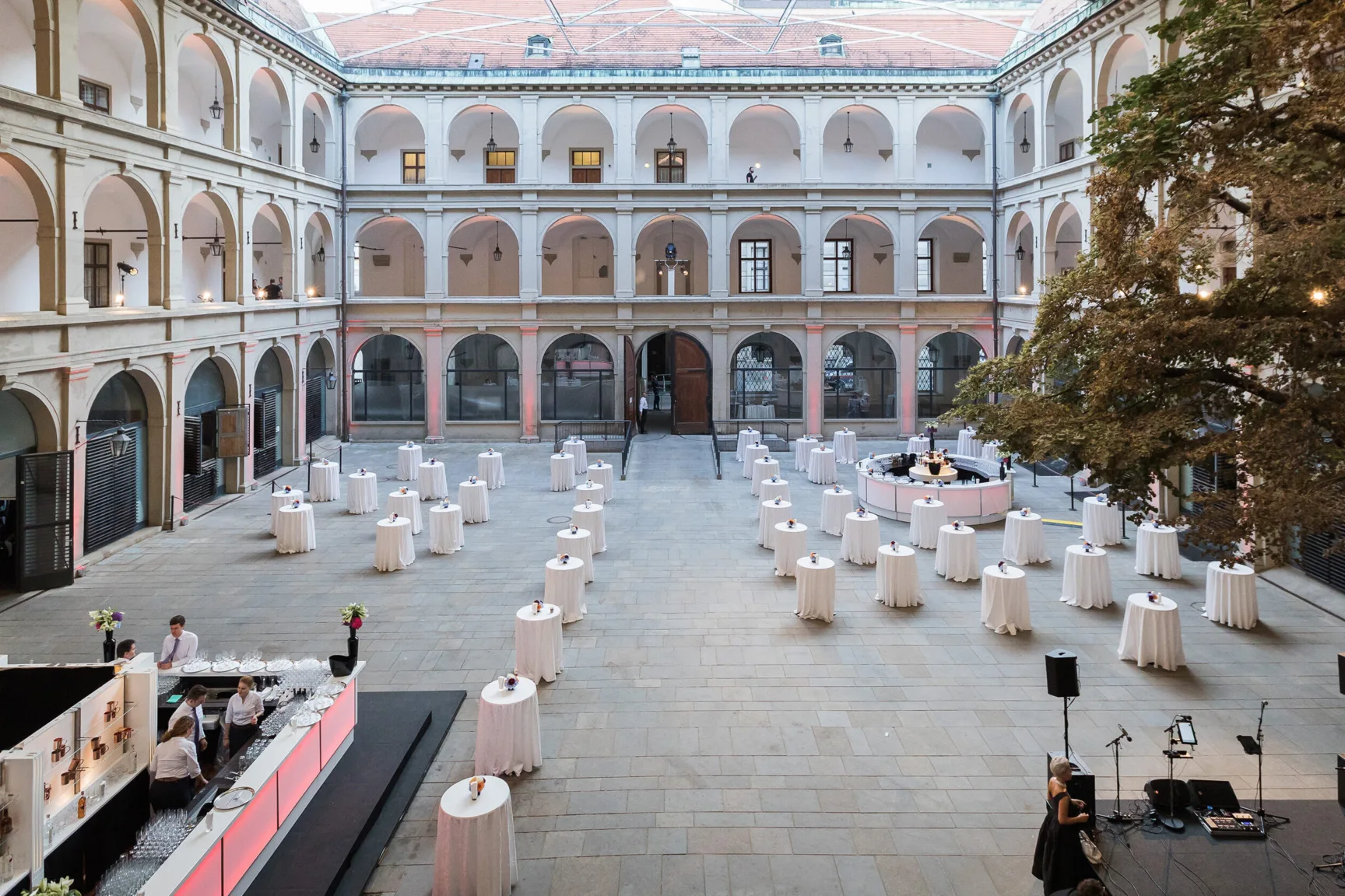 Überdachte Stallburg der Spanischen Hofreitschule, ein Renaissancegebäude mit offenen Arkaden auf zwei Stockwerke. Stehtische in der Mitte und eine Bar.